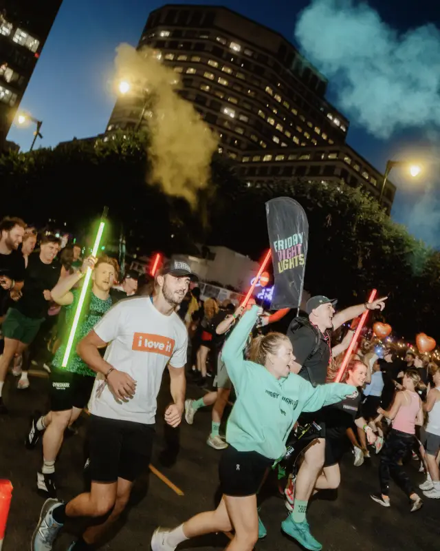 Runners carrying glow sticks and a Friday Night Lights flag through smoke flares on the night course